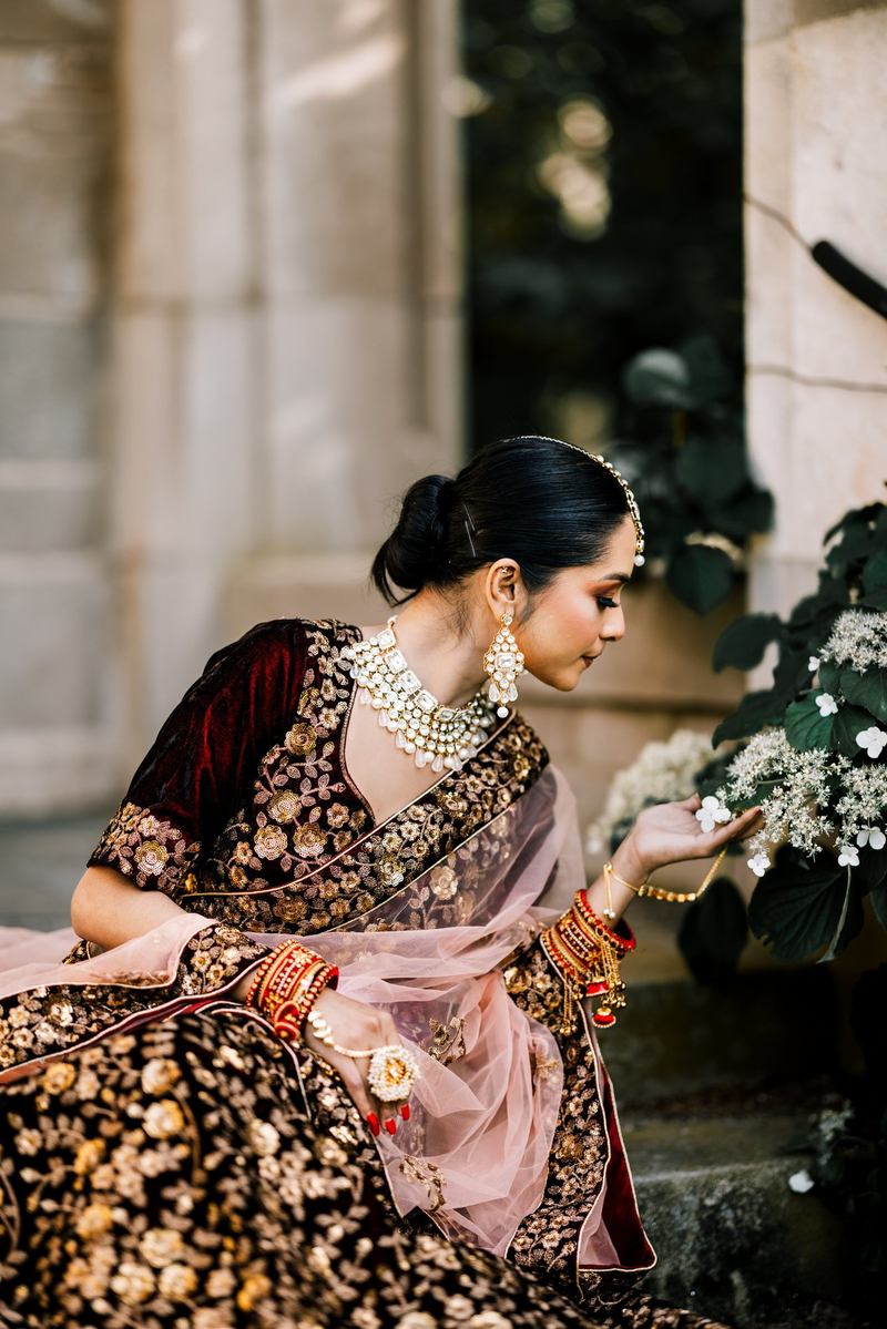 Bride in side profile reaching toward white hydrangeas beside a stone wall