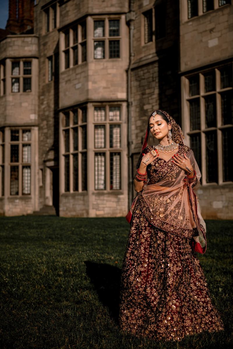 Bride with eyes closed and hands at her chest, standing on a lawn before a stone manor